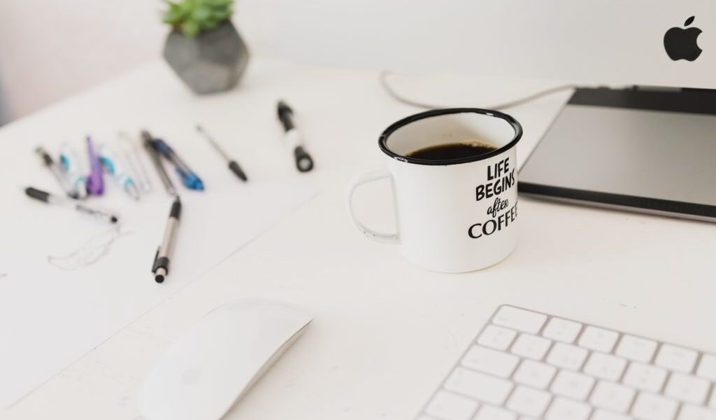 zdjęcie białego biurka a na nim białego kubka, białej myszki i białej klawiatury);