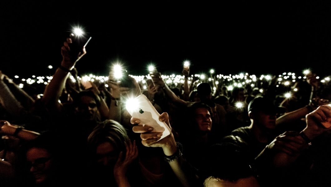 ciemna sala koncertowa i rozświetlający ją błys setek lamp od telefonów);
