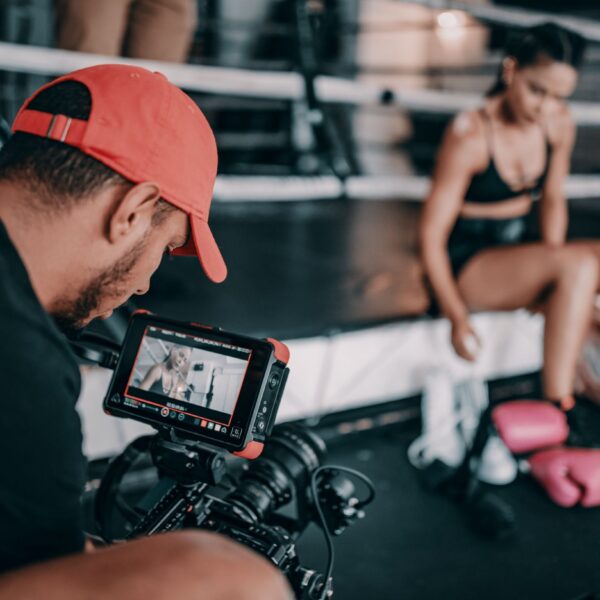 mężczyzna z brodą w czerwonej czapce stoi tyłem, jest za aparatem foto, robi zdjęcie wysportowanej dziewczynie);